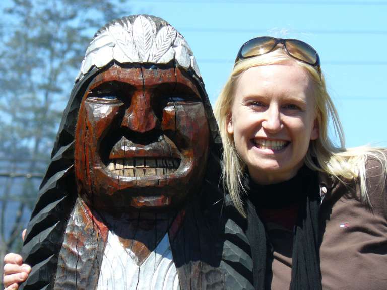 Eine Frau steht neben einer Holzskulptur eines indianischen Mannes