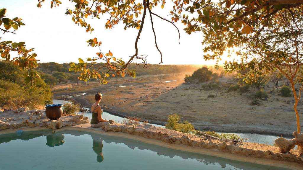 Eine Frau sitzt am Rand eines Pools und schaut auf einen Fluss