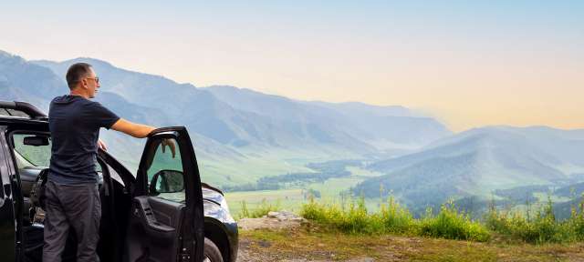 Ein Mann steht neben seinem Auto und schaut auf die Berge